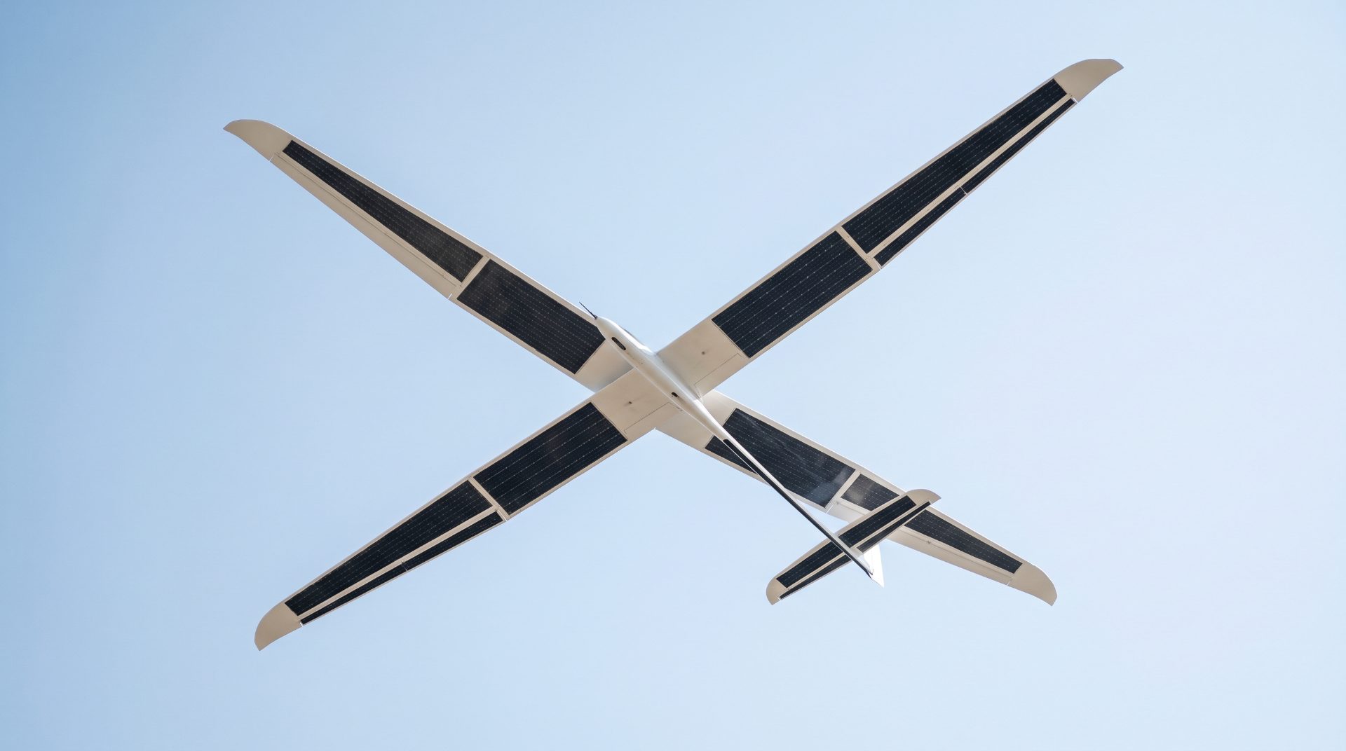 Underside of a wide-span solar aircraft seen against clear sky